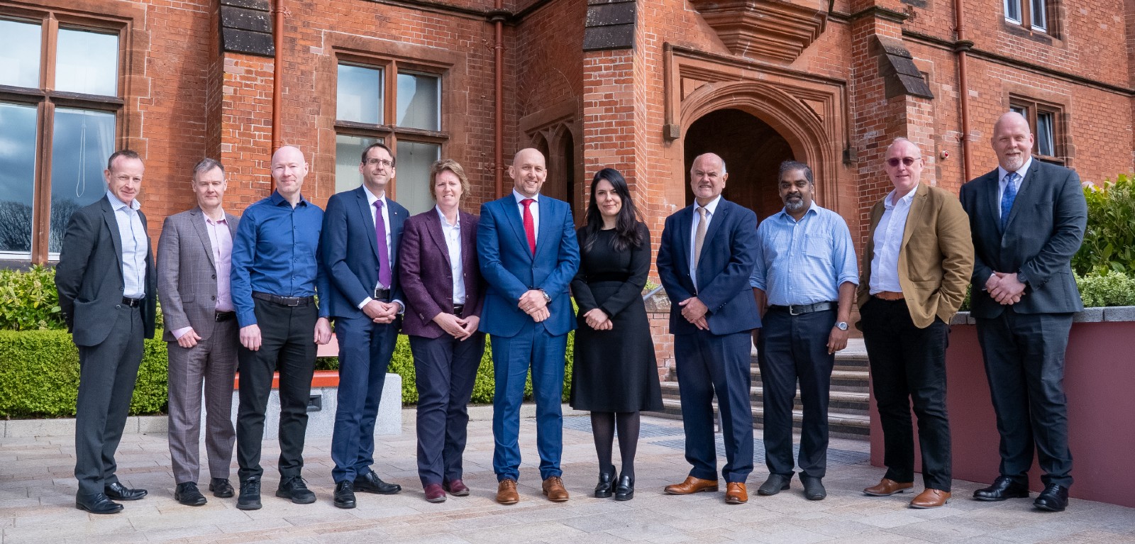 A group of people stand in a lineup outside a historic academic building