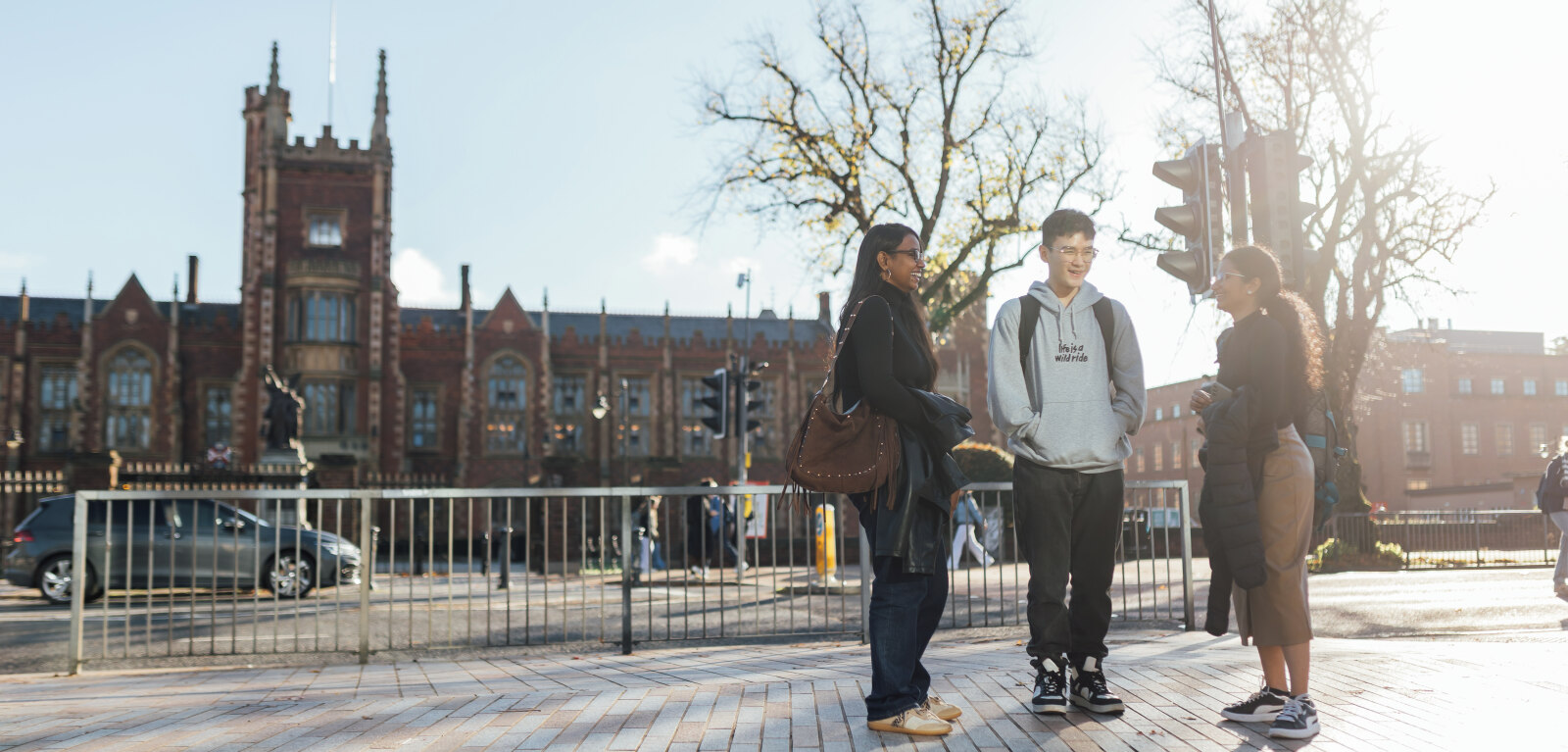 Three students stand together across the road from the Lanyon