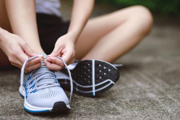 White female sitting down tying white running shoes.