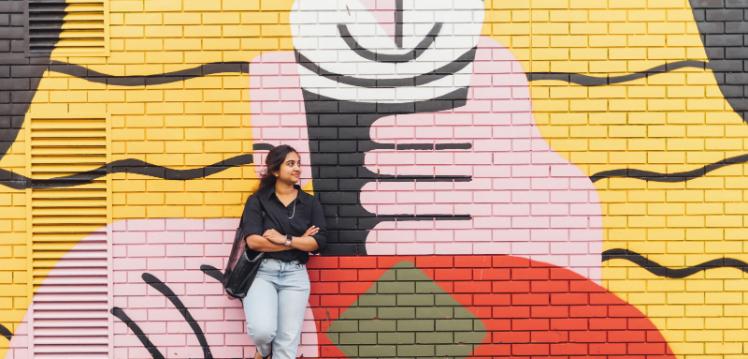 Female student leaning against graffiti art in Belfast