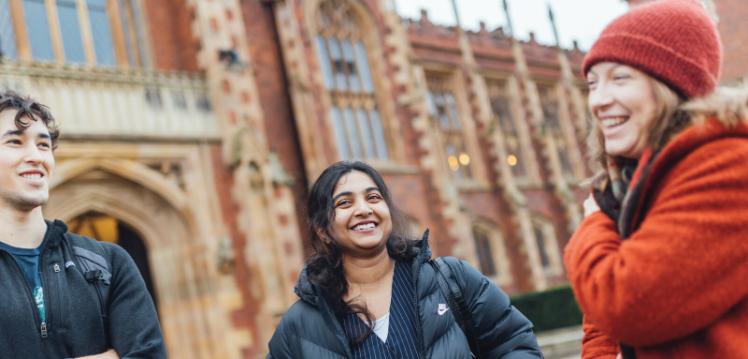 Three students smiling at each other outside Lanyon front