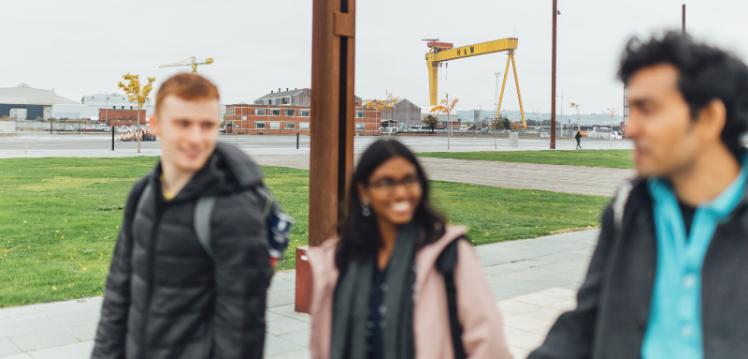 Three students walk in front of yellow crane in Belfast