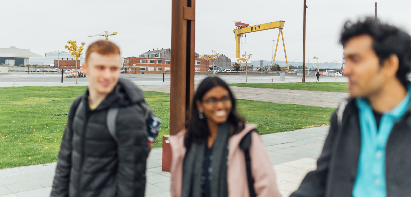 Three students walk in front of yellow crane in Belfast