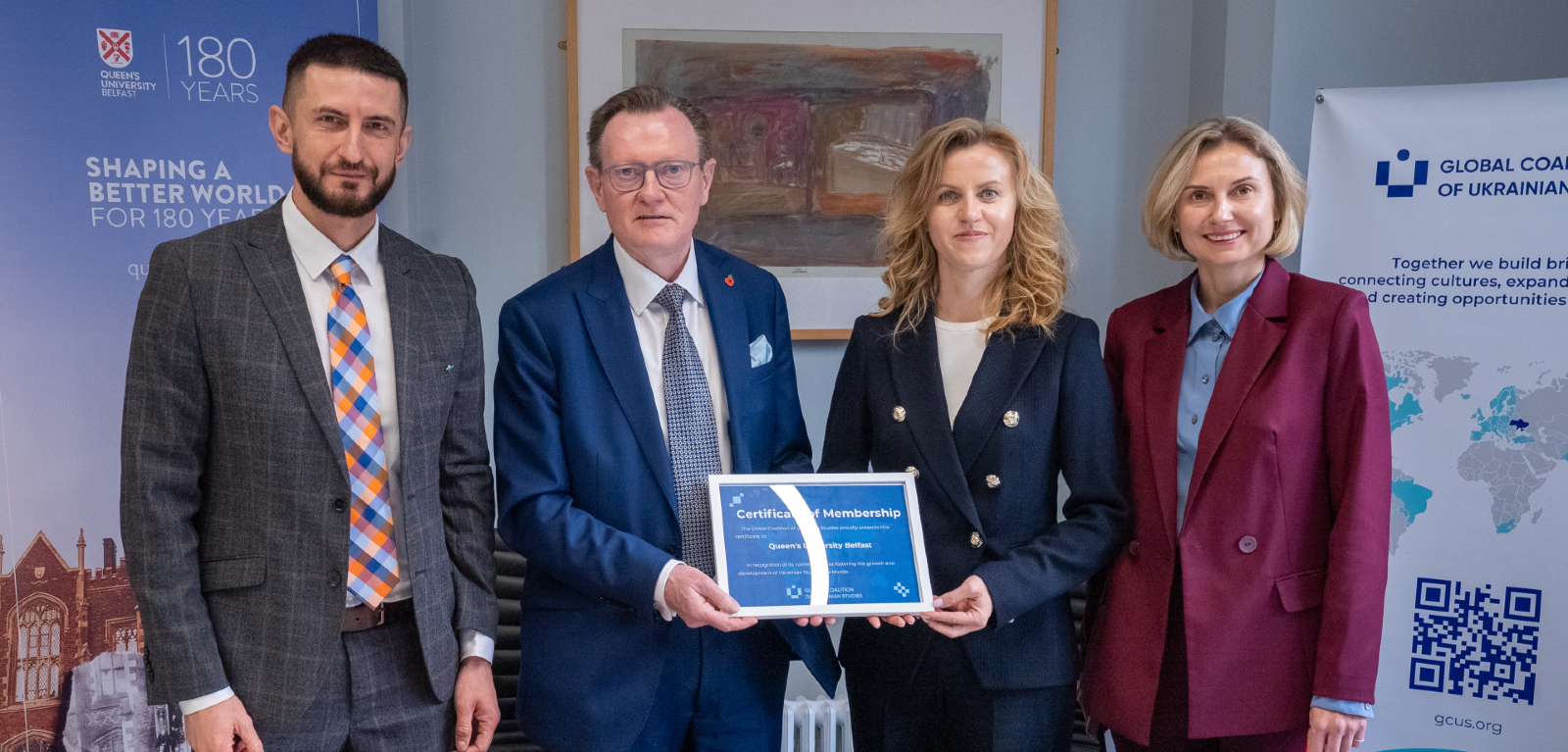 Two men and two women stand posed with a signed agreement document smiling towards the camera