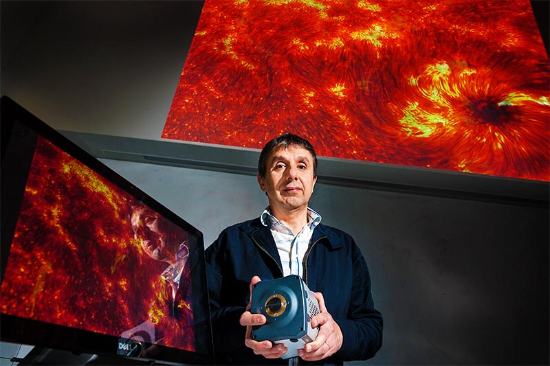 Lecturer with imaging device in front of a large galaxy display