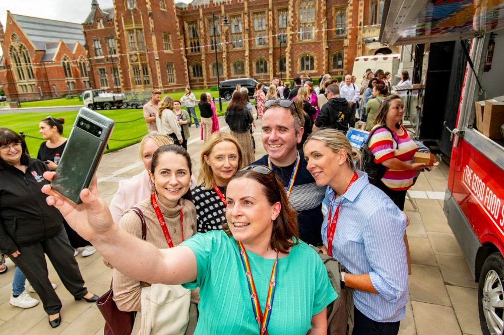 event attendees taking a selfie showing lots of guests, beside food trucks at the Queen's University Belfast Pride Picnic 2024
