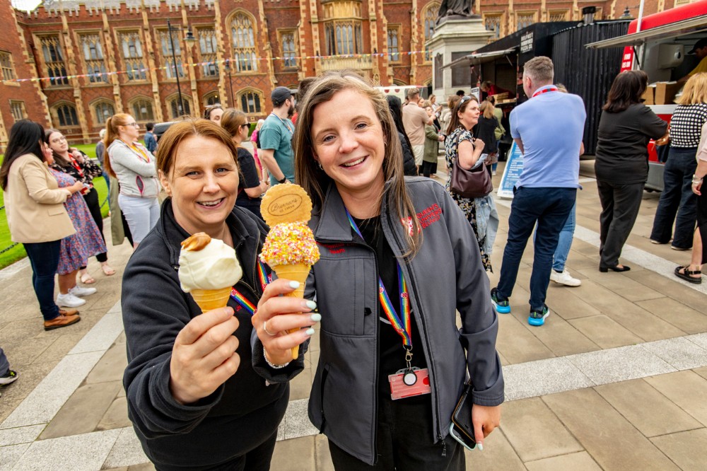 smiling staff holding up ice-cream cones against a background of invited guests outside Queen's Lanyon Building at the Pride Picnic 2024